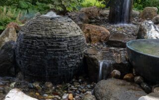 Garden waterfall over rocks with green foliage.