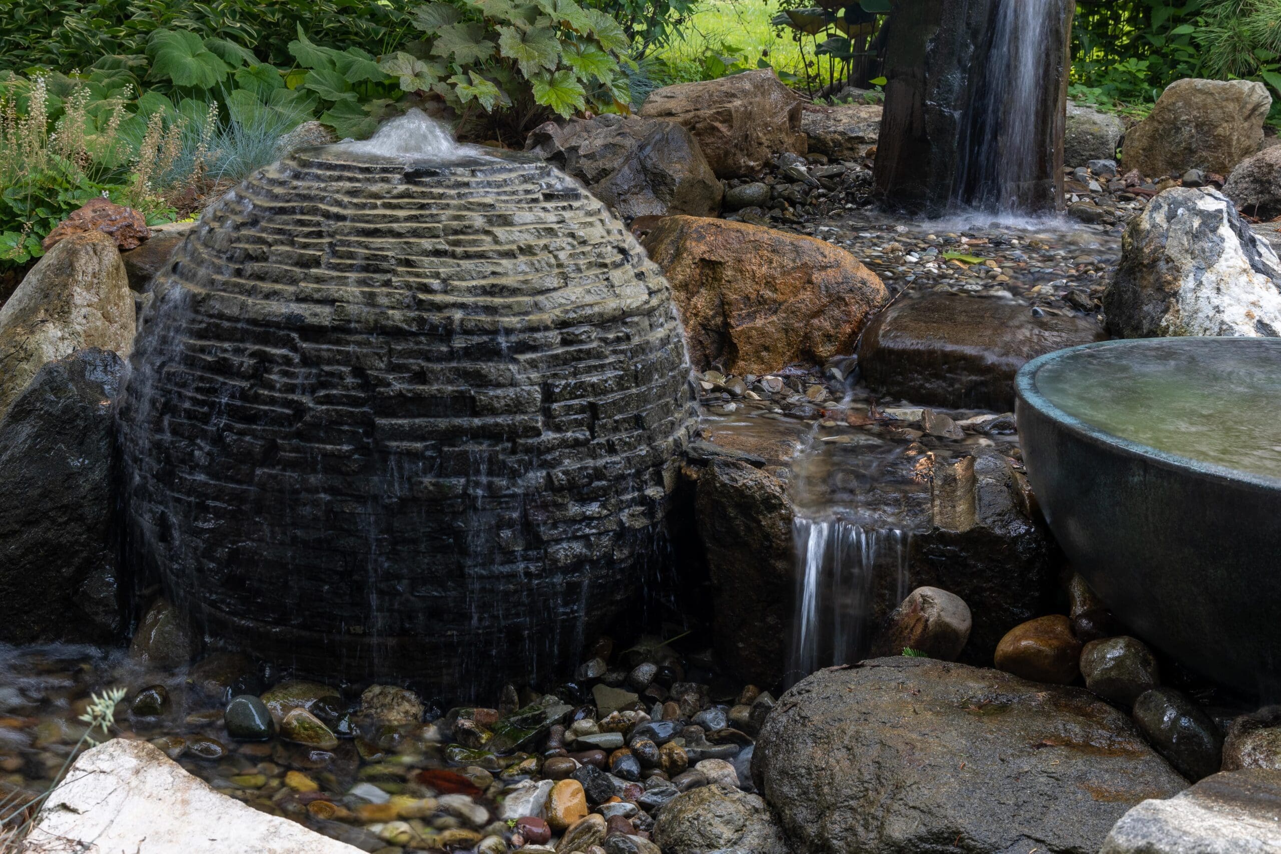 Garden waterfall over rocks with green foliage.