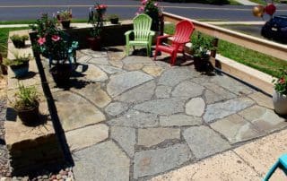 Stone patio with red and green chairs and potted plants