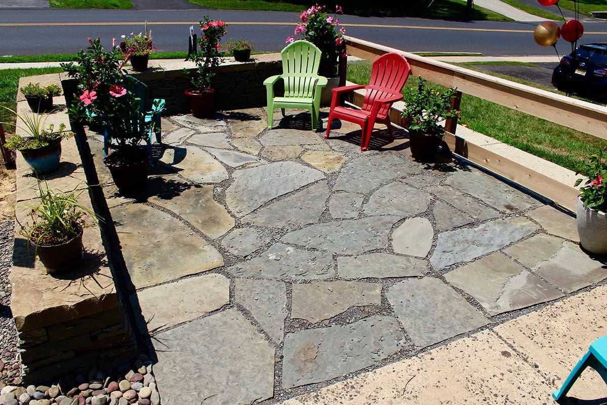 Stone patio with red and green chairs and potted plants