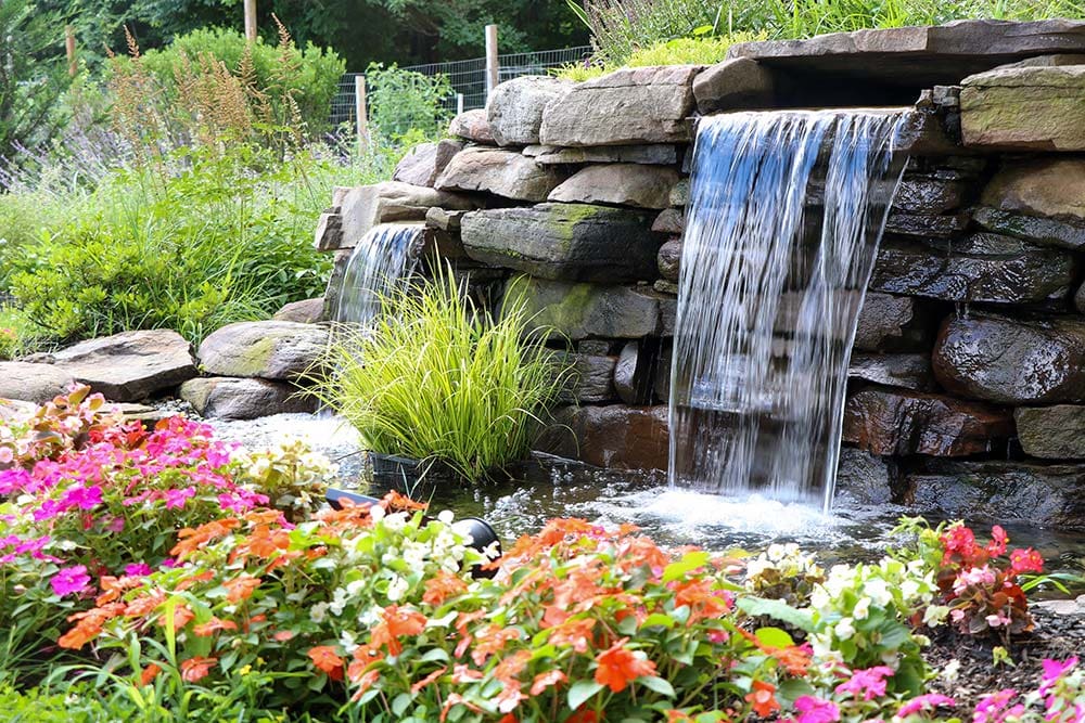 Garden waterfall with colorful flowers and rocks.
