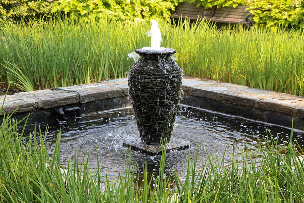 Garden water fountain surrounded by lush greenery.