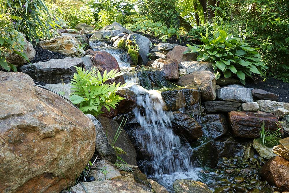 Tranquil garden waterfall over rocks with green foliage.