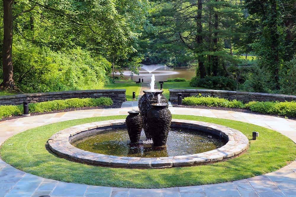 Tranquil garden with stone fountain and greenery.