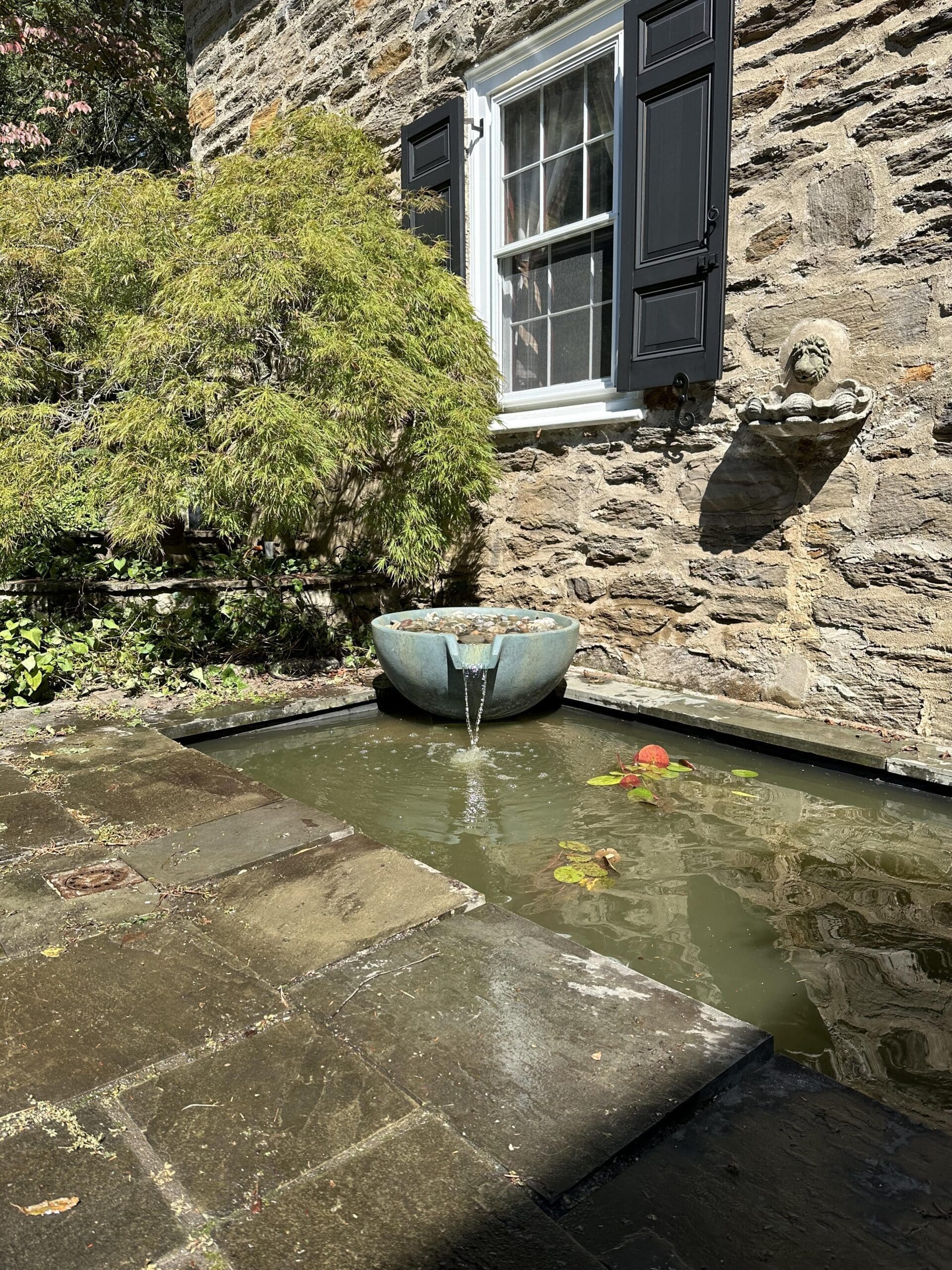 Stone wall with water fountain and pond.